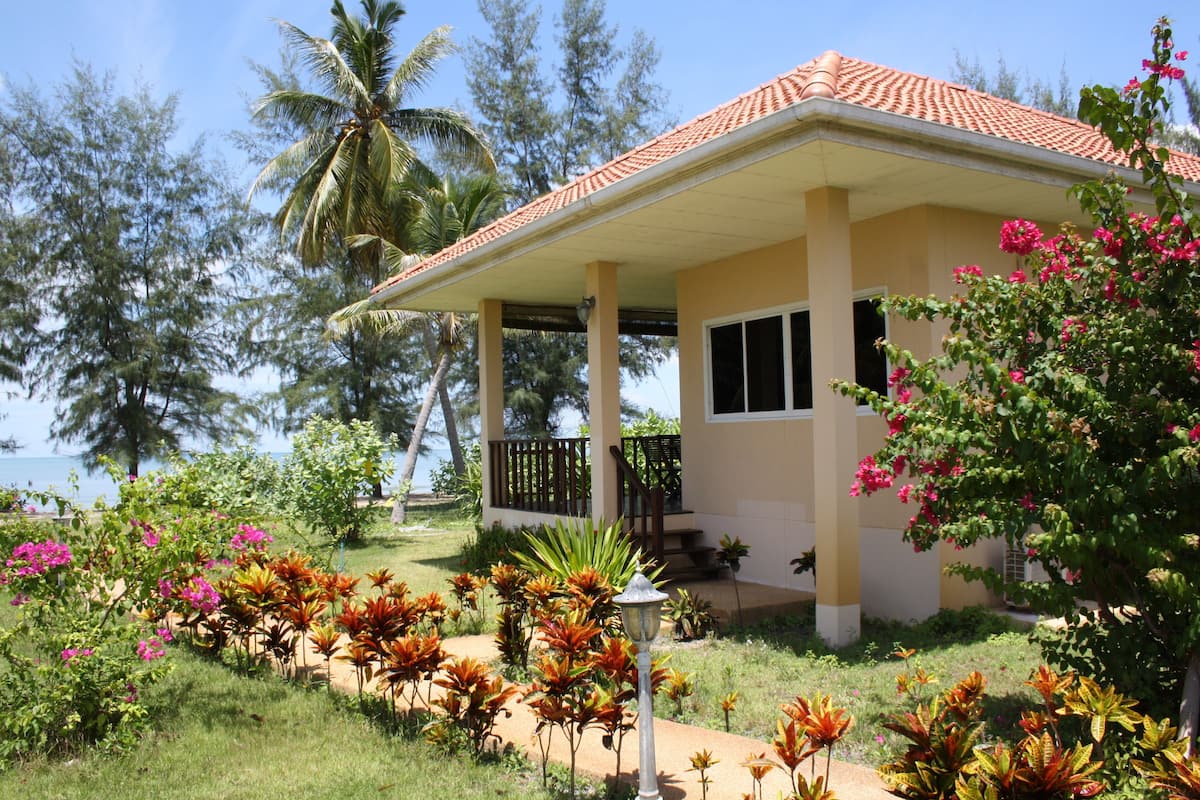 Ein Haus mit einem Ziegeldach, einer Veranda und einem Garten mit verschiedenen Pflanzen und Blumen.