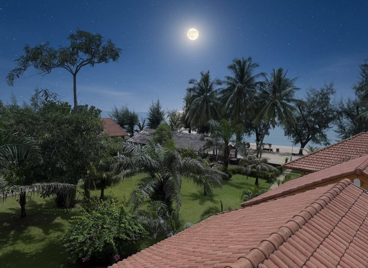 Vista nocturna de un resort con cielo iluminado por la luna, palmeras y un techo de tejas.