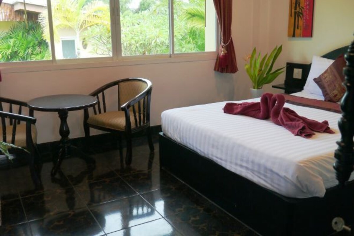 A hotel room with a bed, a chair, a small table, and a view of greenery outside.