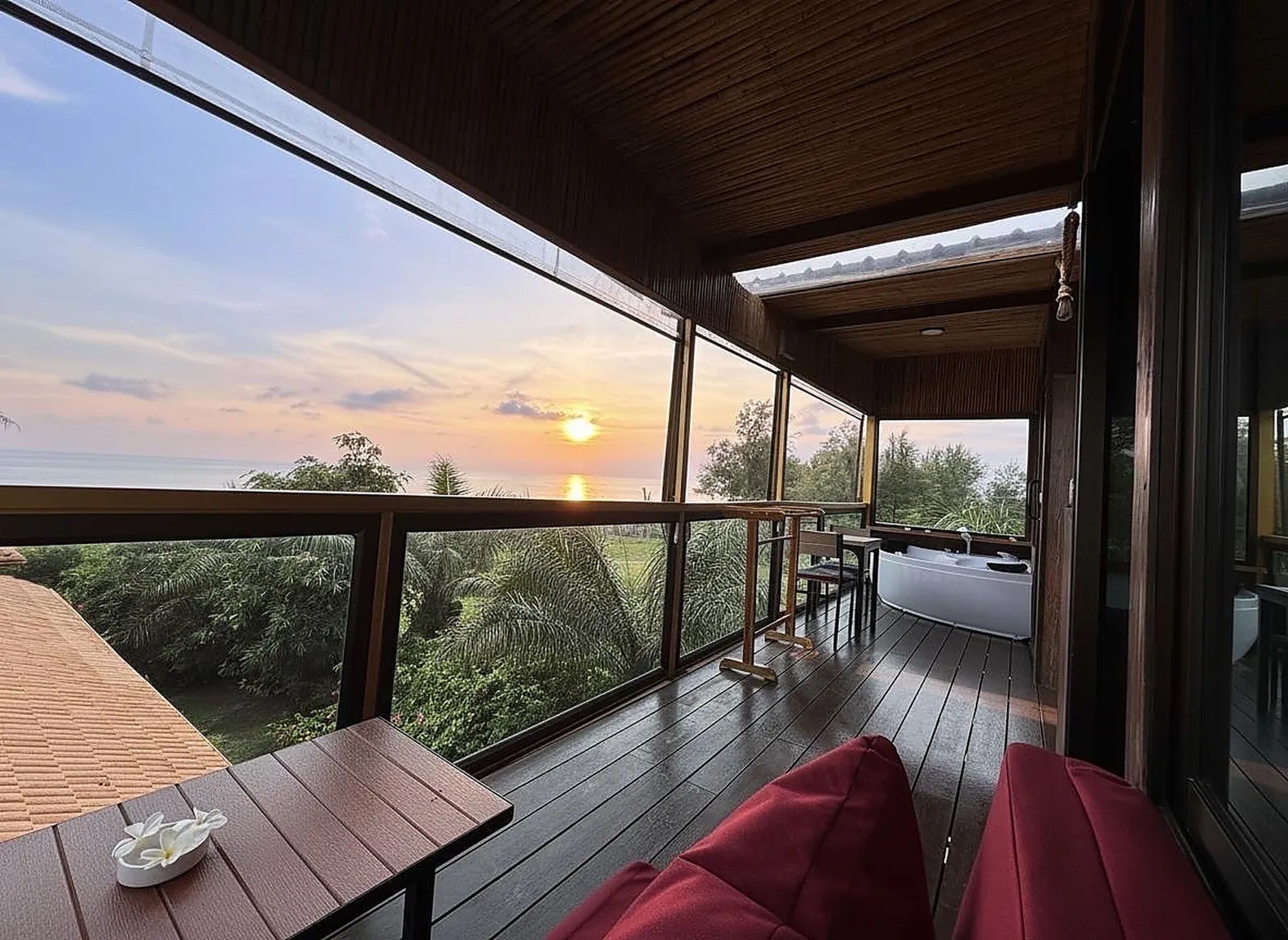 A wooden deck with a view of the sunset, a hot tub, and a table with a flower.