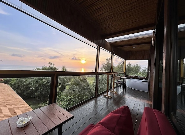 A wooden deck with a view of the sunset, a hot tub, and a table with a flower.