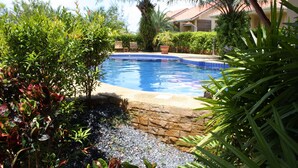 Una piscina rodeada de abundante vegetación y un muro de piedra.