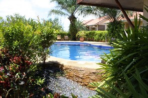 A swimming pool surrounded by lush greenery and a stone wall. - Ao Thai Resort (Sathing Phra)