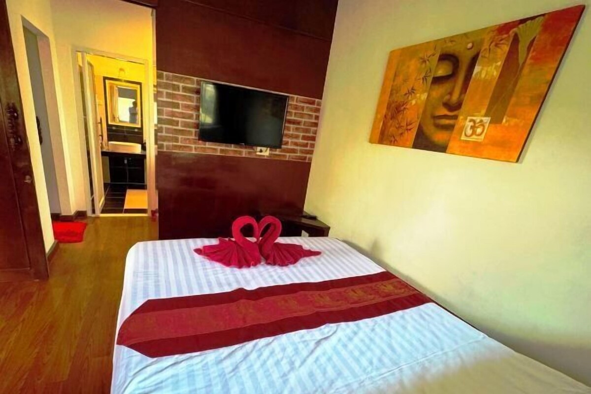 A hotel room with a bed, a television mounted on a brick wall, and a painting on the wall.