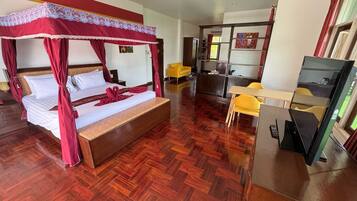 A hotel room with a four-poster bed, a desk with a chair, and a television.