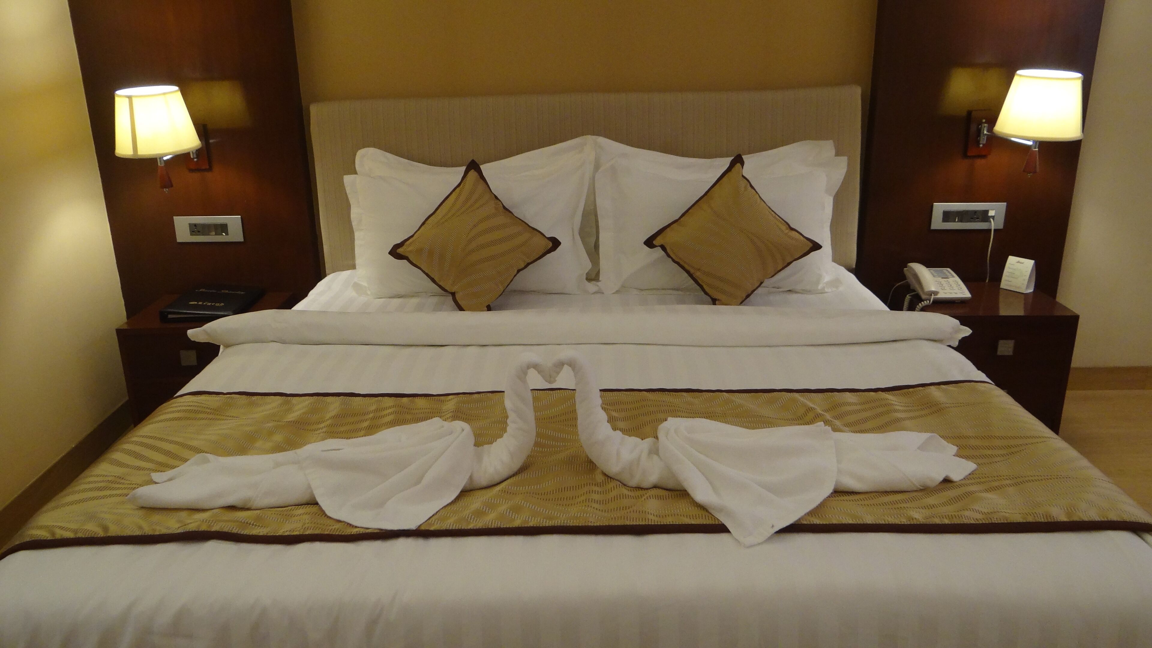 Une chambre d’hôtel avec un lit soigneusement fait, deux lampes fixées au mur, un téléphone sur la table de chevet et une petite table avec un livre et un bloc-notes.