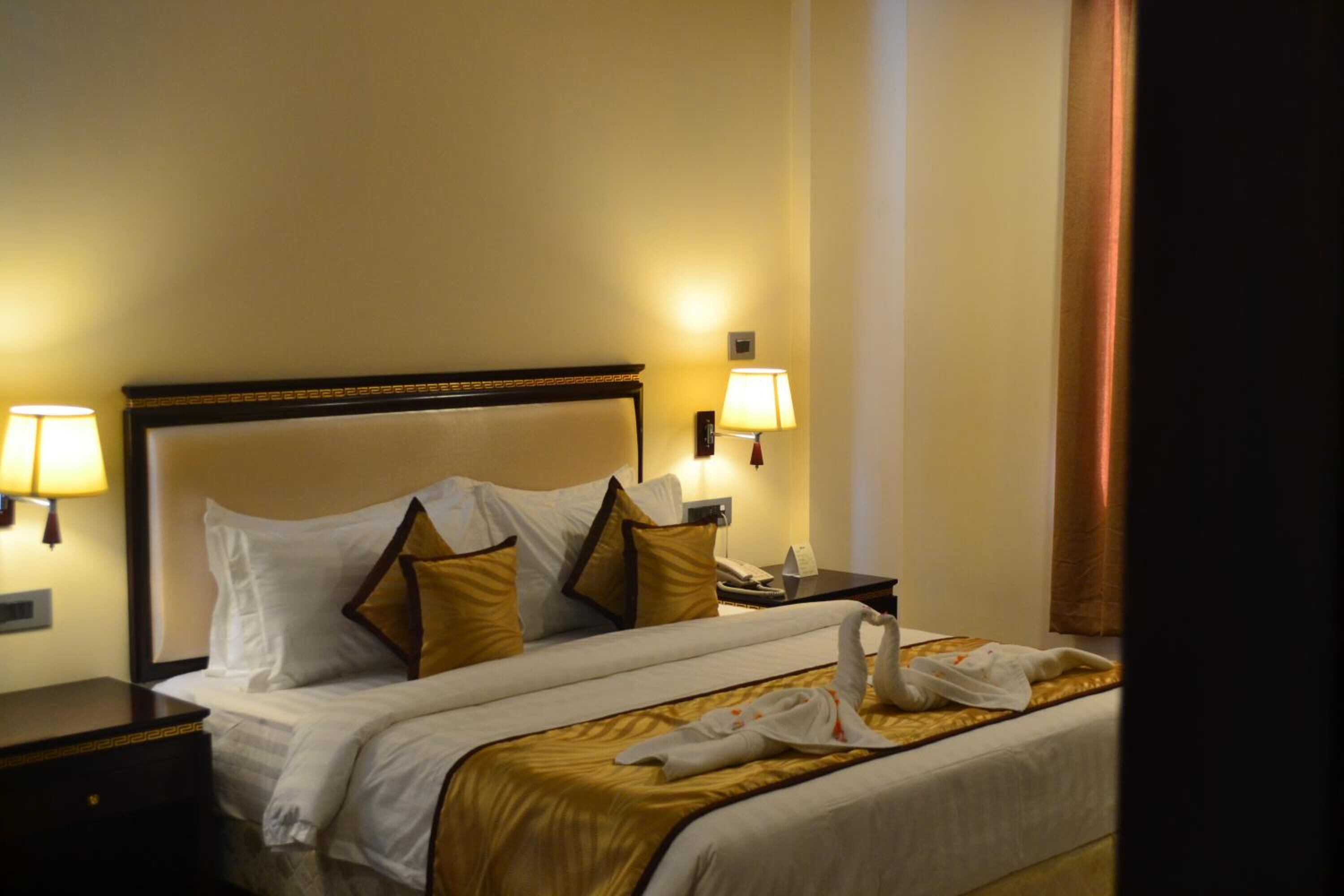 Una habitación de hotel con una cama grande, dos lámparas de noche, una mesita de noche y un teléfono instalado en la pared.