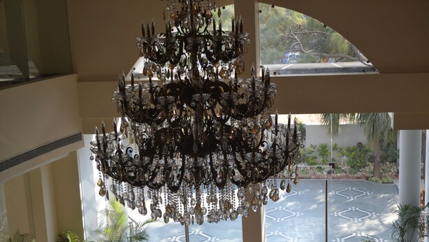A grand chandelier in a spacious lobby with a view of a courtyard. - The Legend Hotel (Prayagraj)