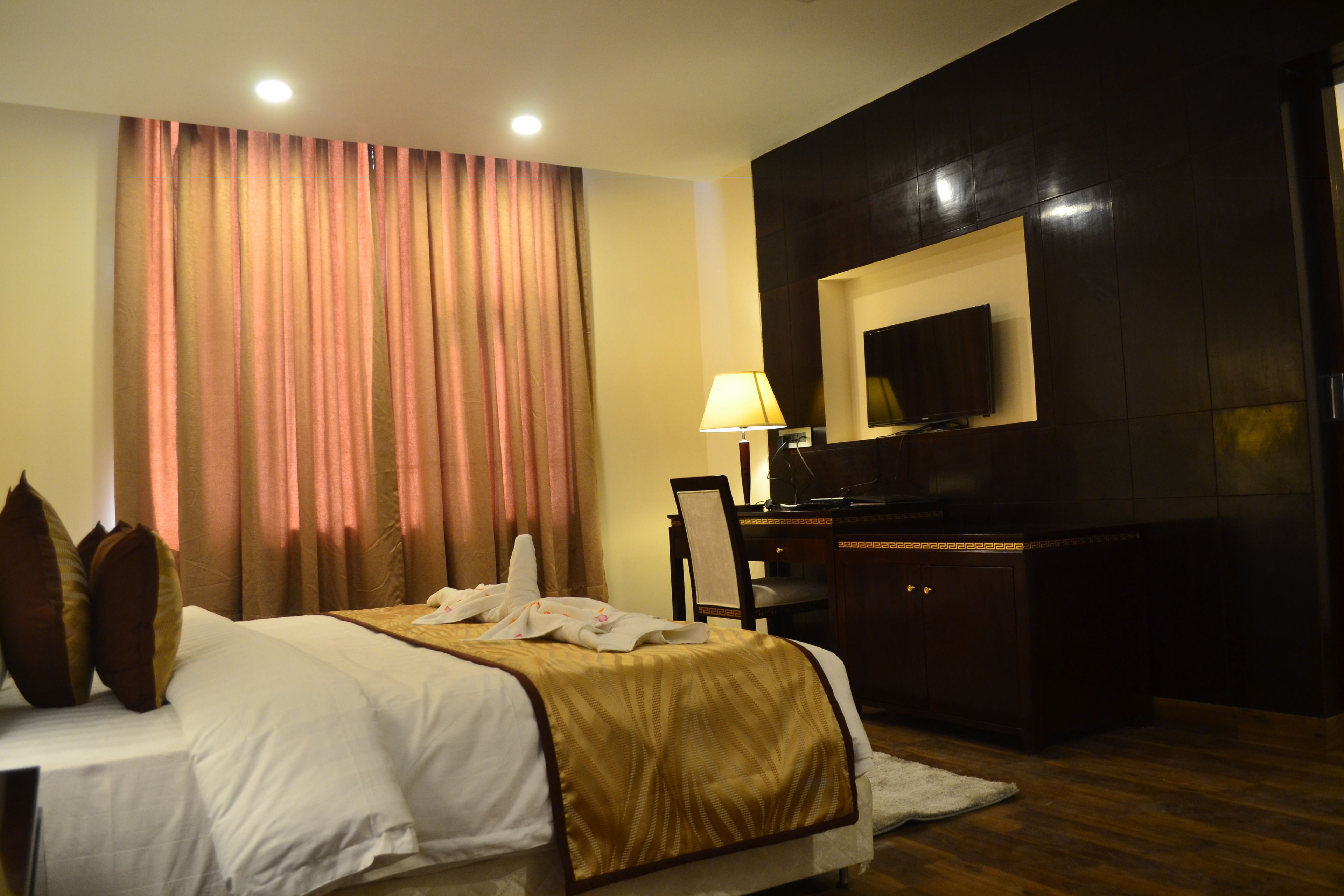 A hotel room with a bed, a desk, a chair, a TV, and a large window with curtains.