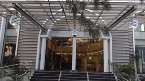 A modern building entrance with a covered entrance area, steps leading up to the entrance, and potted plants around the entrance. - The Legend Hotel (Prayagraj)