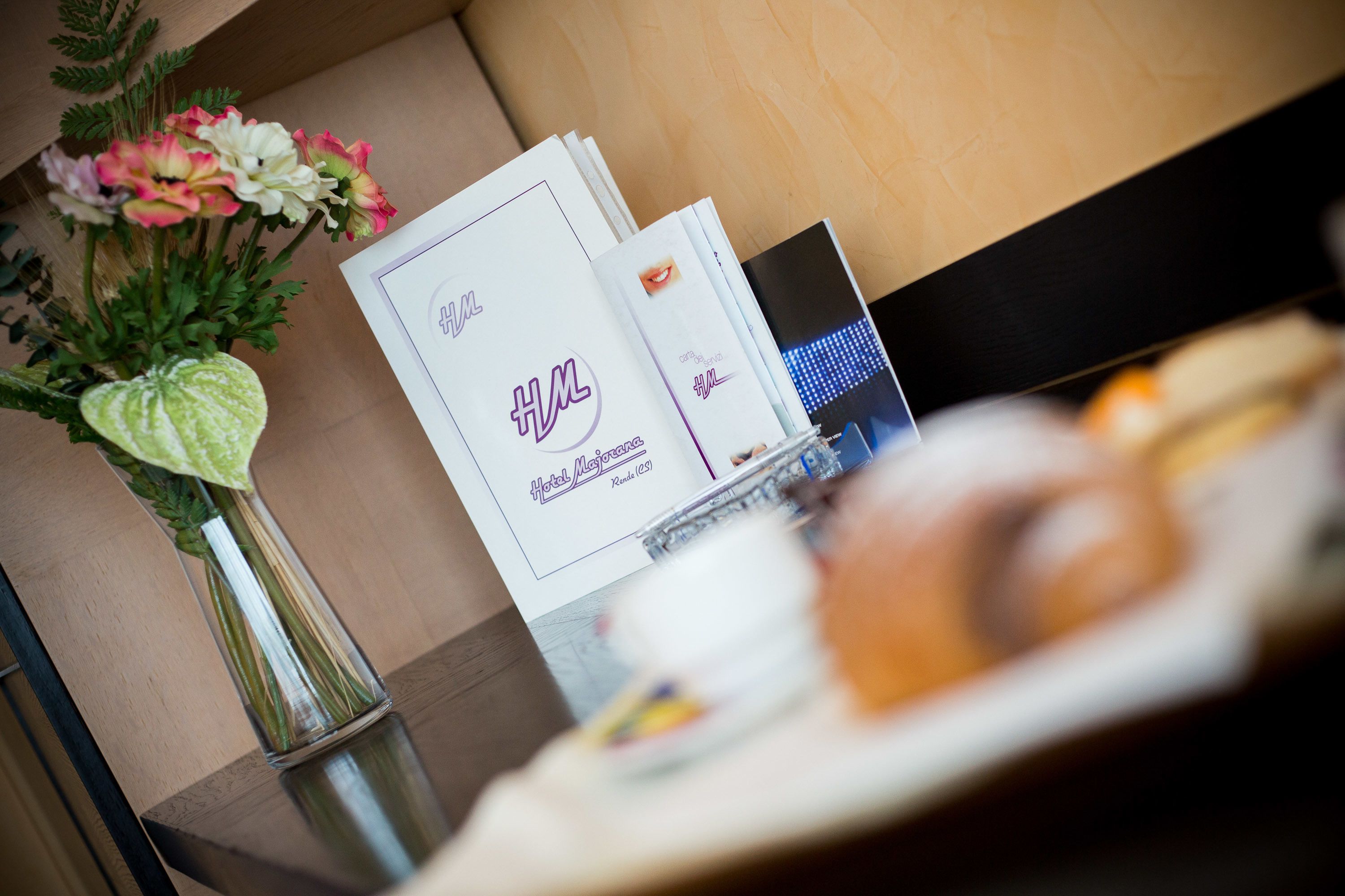 Une brochure d’hôtel, un vase rempli de fleurs et une assiette avec des aliments, le tout posé sur une table.