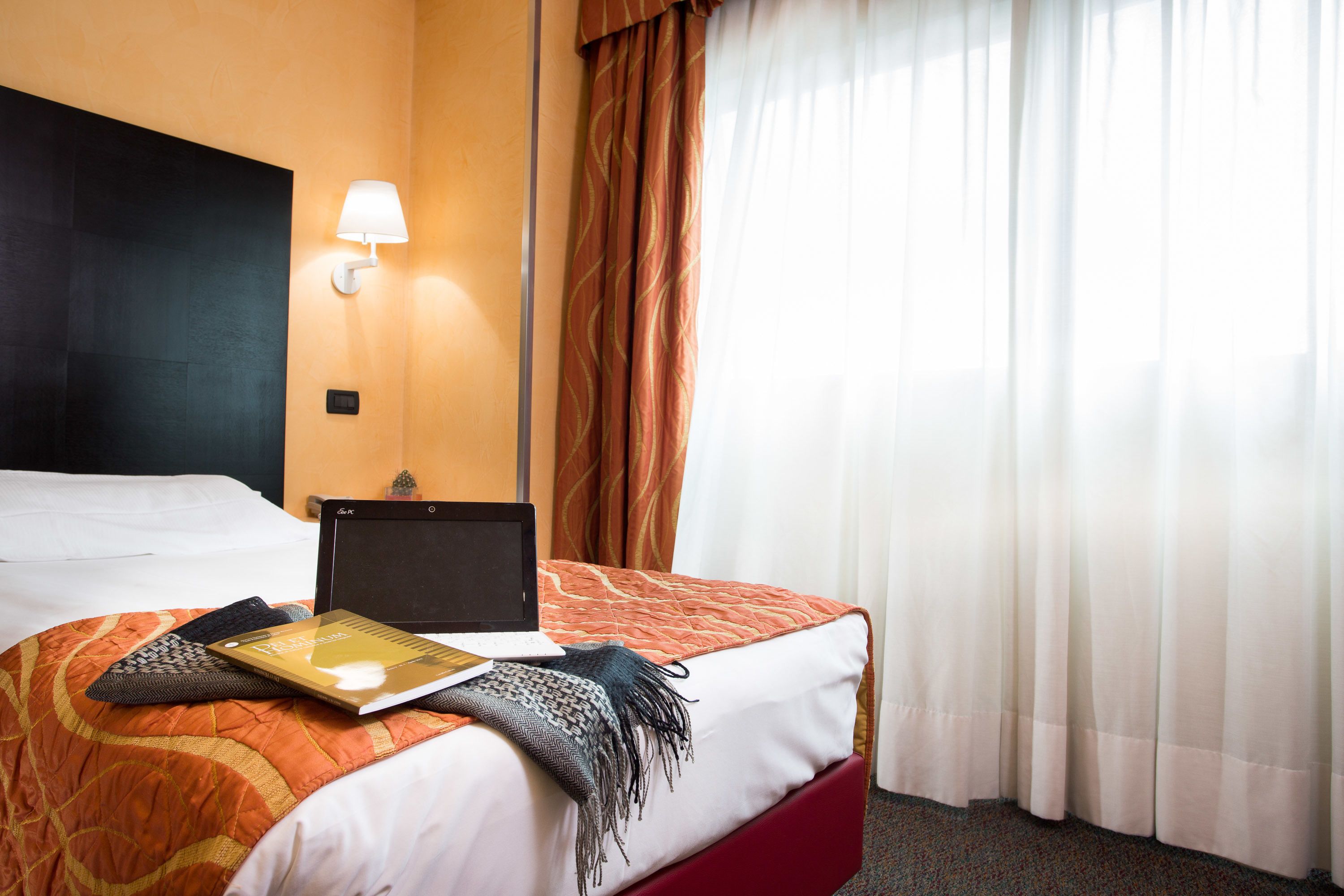 A hotel room with a bed, a laptop, a book, and a lamp.