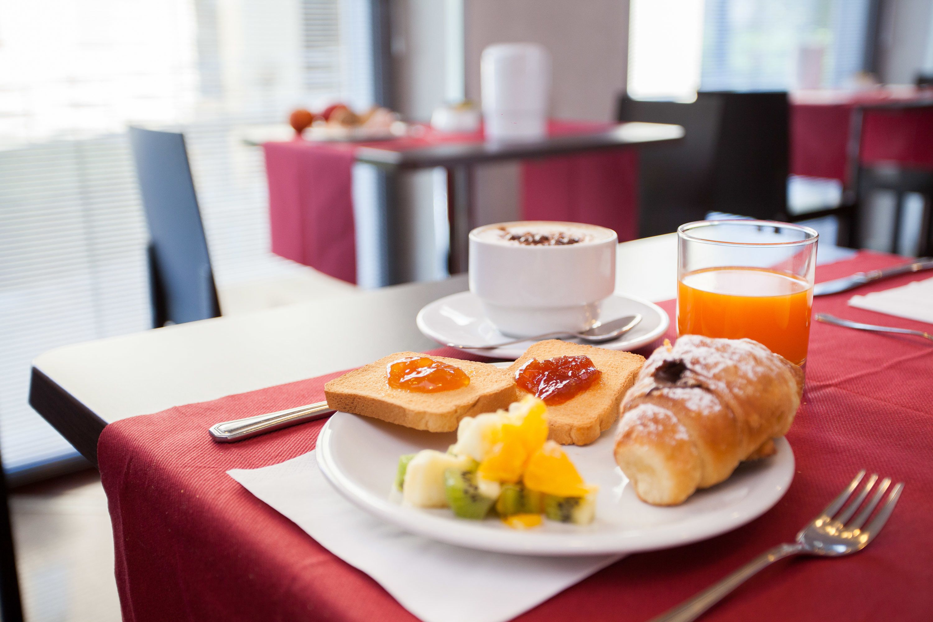 Et morgenbord med ristet brød, marmelade, en croissant og et glas appelsinjuice på et bord.