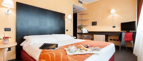 Habitación de hotel con cama, escritorio, silla, televisor y bandeja con alimentos para el desayuno.