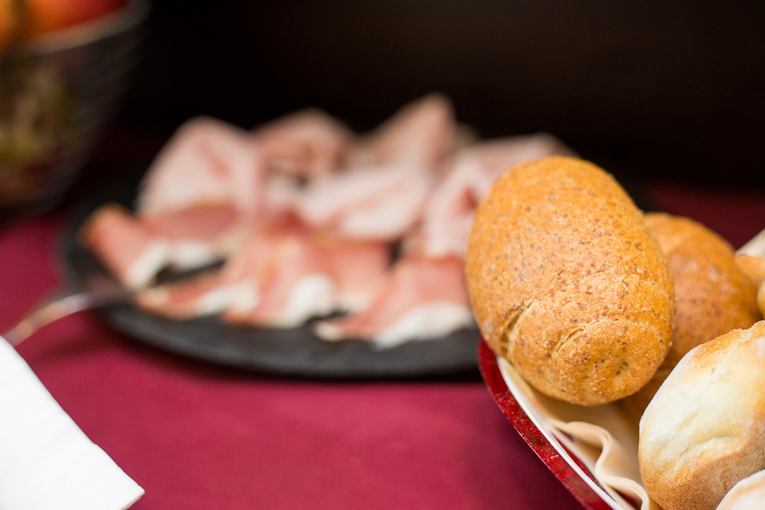 A table with a plate of sliced meats and a basket of bread rolls.