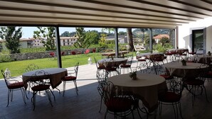 An outdoor dining area with tables and chairs, large windows, and a view of greenery and buildings. - Podere Castel Merlo Resort (Villongo)