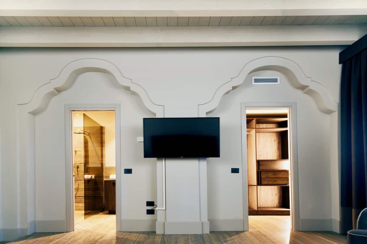A room with a flat-screen TV mounted on a white wall, flanked by two doors leading to a bathroom and a closet.