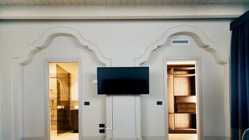 A room with a flat-screen TV mounted on a white wall, flanked by two doors leading to a bathroom and a closet.