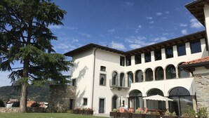 A two-story building with a white facade, stone foundation, and a courtyard with outdoor seating. - Podere Castel Merlo Resort (Villongo)