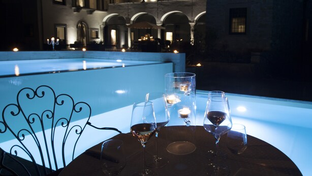 A table with wine glasses and candles, overlooking a courtyard with arched windows and a pool. - Podere Castel Merlo Resort (Villongo)
