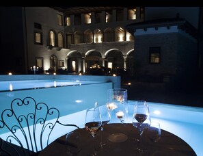 A table with wine glasses and candles, overlooking a courtyard with arched windows and a pool. - Podere Castel Merlo Resort (Villongo)