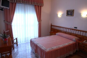 A bedroom with a bed, a desk with a computer, a chair, a potted plant, and a window with curtains. - Hotel JR (Sanxenxo)