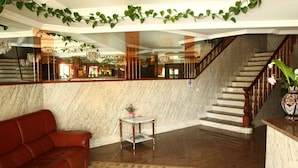 A lobby with a marble floor, a red leather sofa, a small table with a vase, and a staircase. - Hotel JR (Sanxenxo)