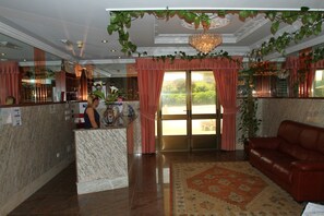 A lobby with a reception desk, a red leather sofa, a chandelier, and a large window with curtains. - Hotel JR (Sanxenxo)