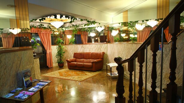 A lobby with a marble floor, a brown leather sofa, a small table with brochures, and a staircase with wooden balusters. - Hotel JR (Sanxenxo)