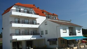 A two-story building with a white facade, balconies, a cafe with outdoor seating, and a sign indicating a hotel and restaurant. - Hotel JR (Sanxenxo)