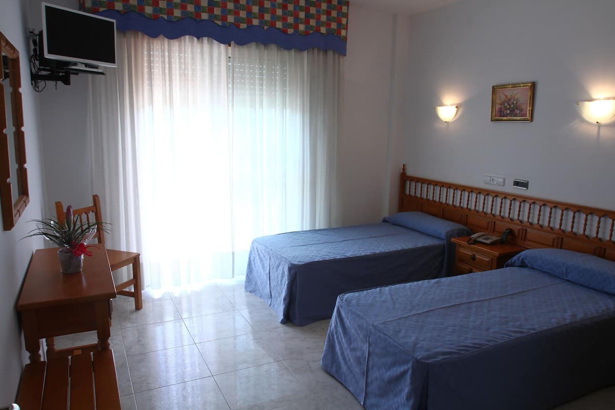 A hotel room with two beds, a TV mounted on the wall, a desk with a chair, and a potted plant.