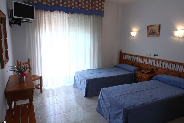 Habitación de hotel con dos camas, un televisor montado en la pared, un escritorio con una silla y una planta en maceta.