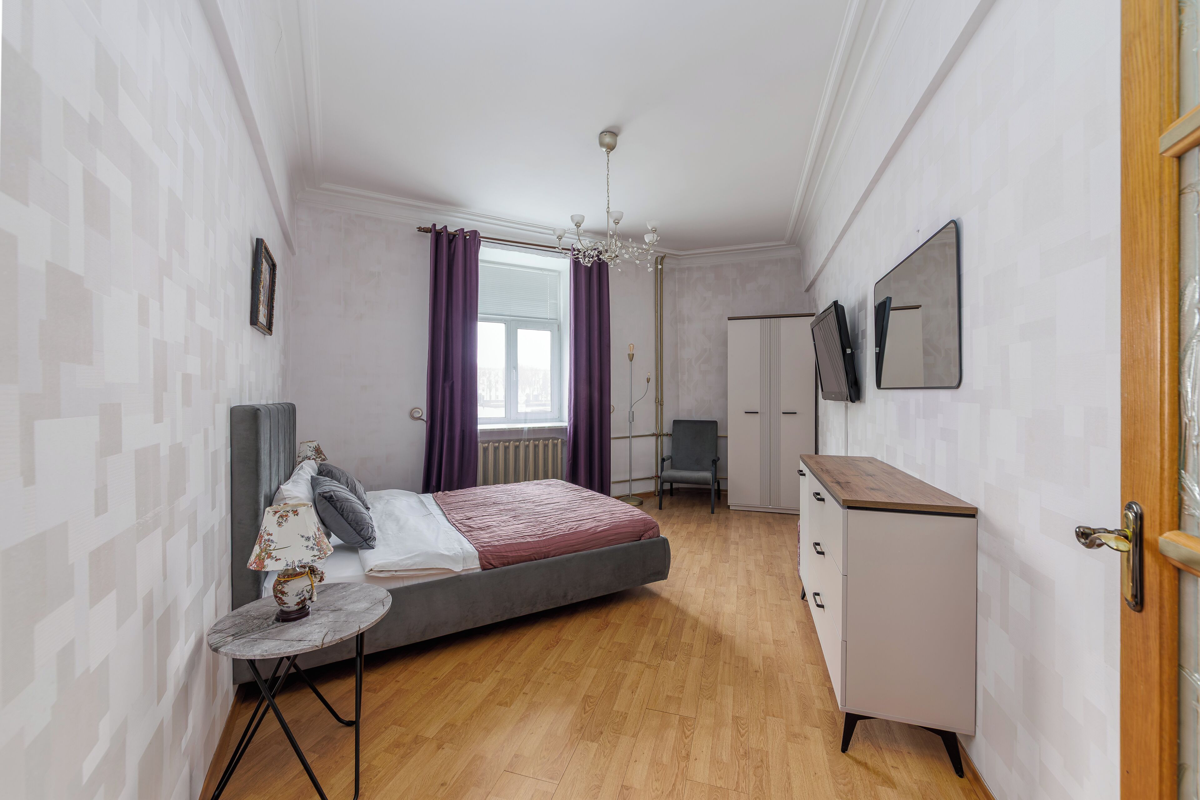A bedroom with a bed, a desk, a chair, a wardrobe, and a mirror on the wall.