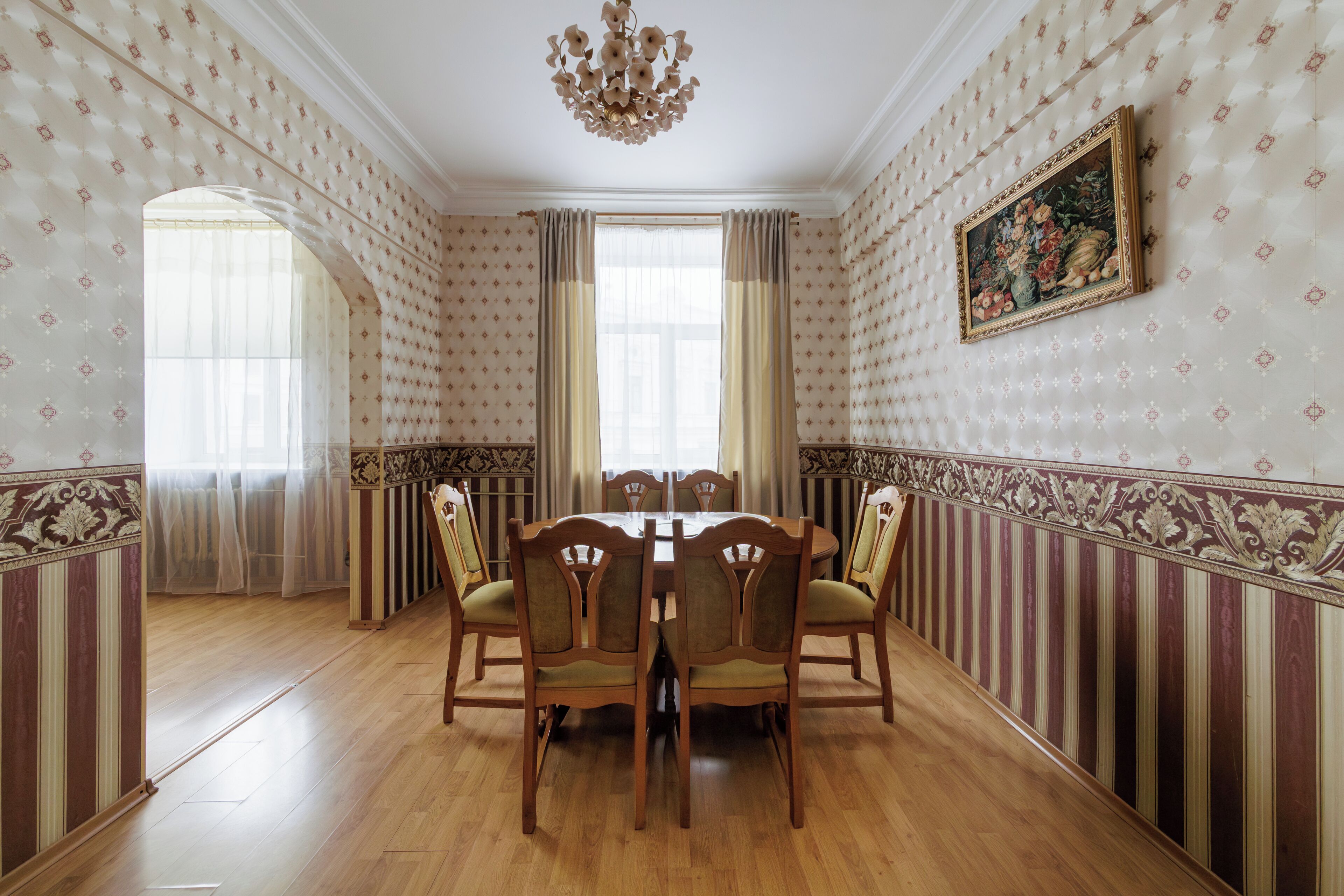 A dining room with a wooden table and chairs, a chandelier, patterned wallpaper, and a painting on the wall.