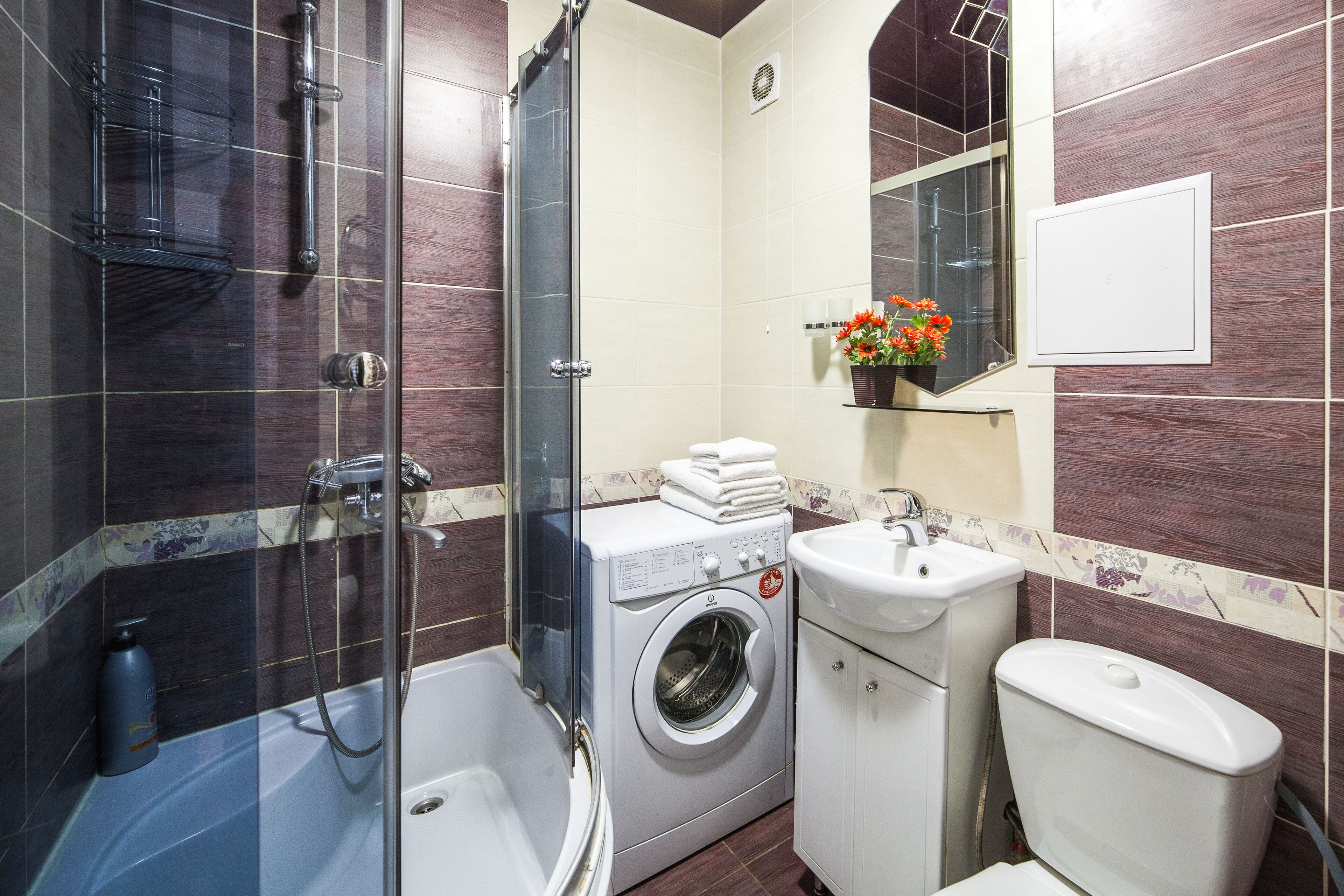 A modern bathroom with a glass-enclosed shower, a washing machine, a toilet, and a sink.