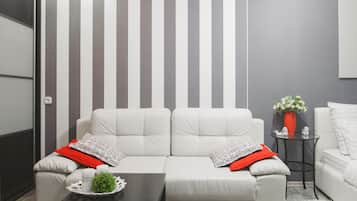 A modern living room with a striped wall, a white sofa set, a small table with a tray, and a vase with flowers.