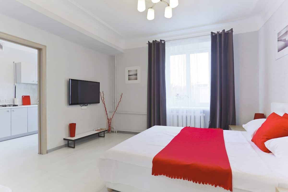 Une chambre d’hôtel moderne dotée d’un grand lit, d’un téléviseur à écran plat, d’un petit coin salon et offrant une vue sur la ville par la fenêtre.