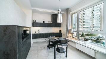 A modern kitchen with a dining area, a large window with a view of a cityscape, and a pendant light.