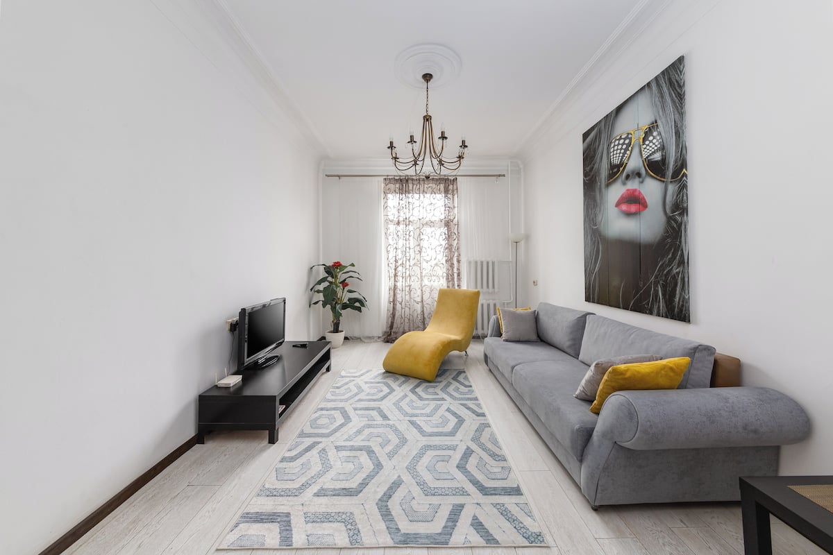 Un salon avec un canapé, un fauteuil jaune, un téléviseur et un lustre.