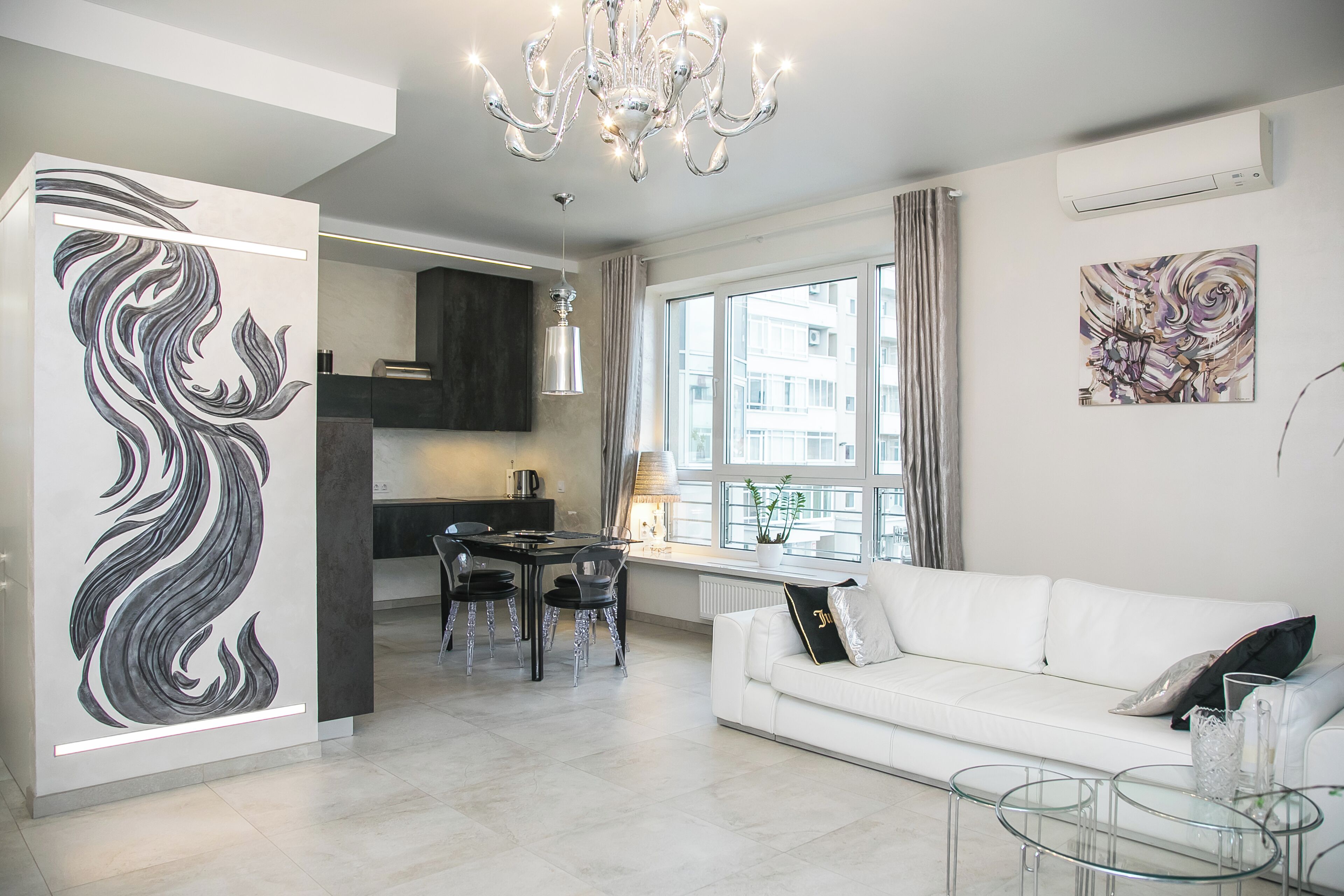 A modern living room with a white sofa, a glass coffee table, and a dining area with a chandelier.