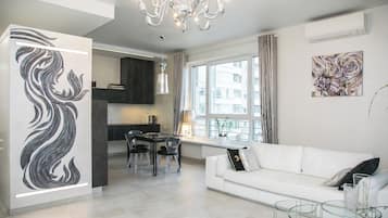 A modern living room with a white sofa, a glass coffee table, and a dining area with a chandelier.