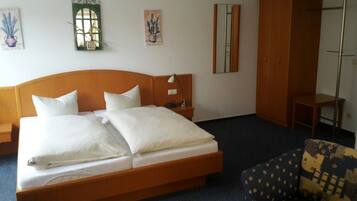 A hotel room with a large bed, a wardrobe, a chair, and two wall-mounted mirrors.