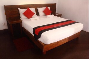 A neatly made bed with white linens and red and black accents, a wooden headboard, and a small bedside table with a red rug. - 256 Townhouse Rest (Kandy)