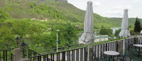 A terrace with outdoor seating, a view of a river, and a mountain in the background.