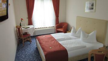 Habitació d'hotel amb un llit, escriptori, cadira, finestra amb cortines i un quadre a la paret.