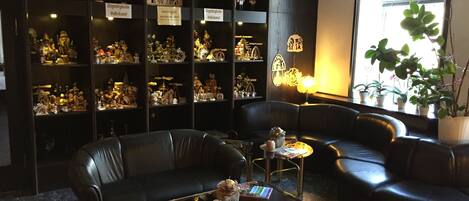 A cozy room with leather sofas, a glass coffee table with newspapers, and shelves filled with various items.