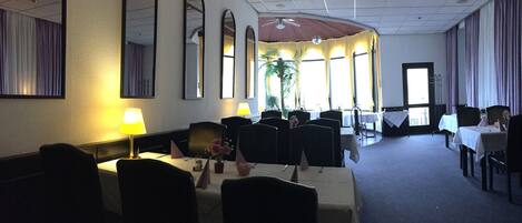A hotel dining area with tables, chairs, and a ceiling fan.