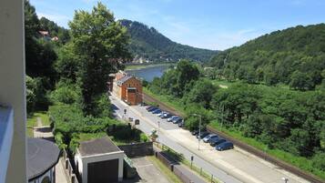 A parking area with cars, a building with a red roof, and a view of a river and hills.