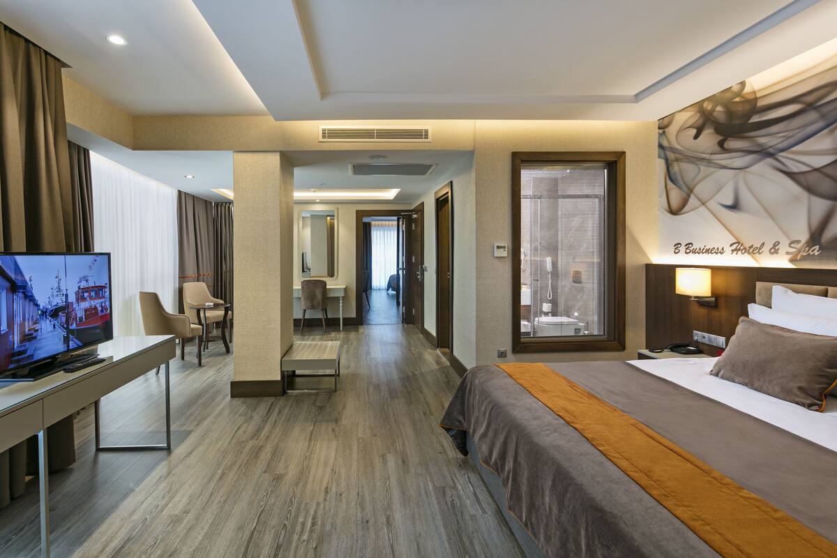 A hotel room with a bed, a desk with a TV, and a bathroom visible through an open door.