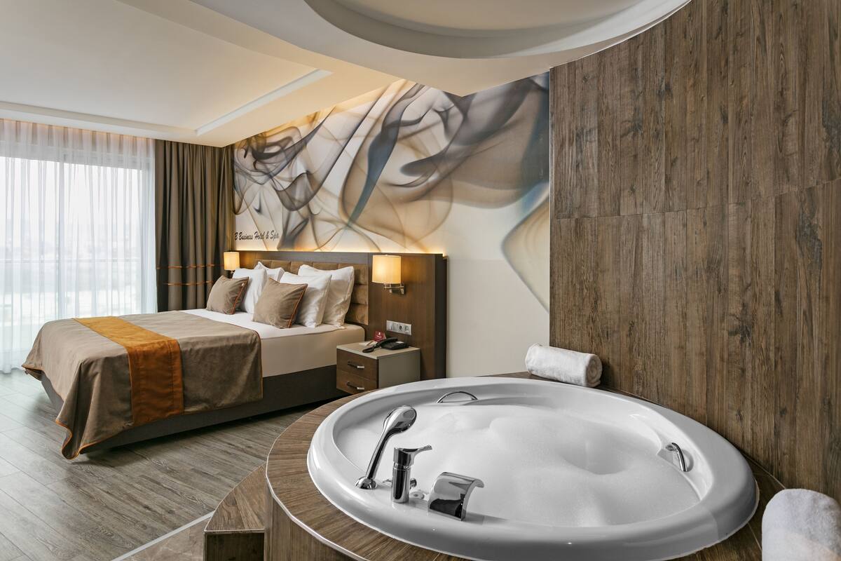 A modern hotel room with a large bed, a built-in bathtub, and a wall mural.
